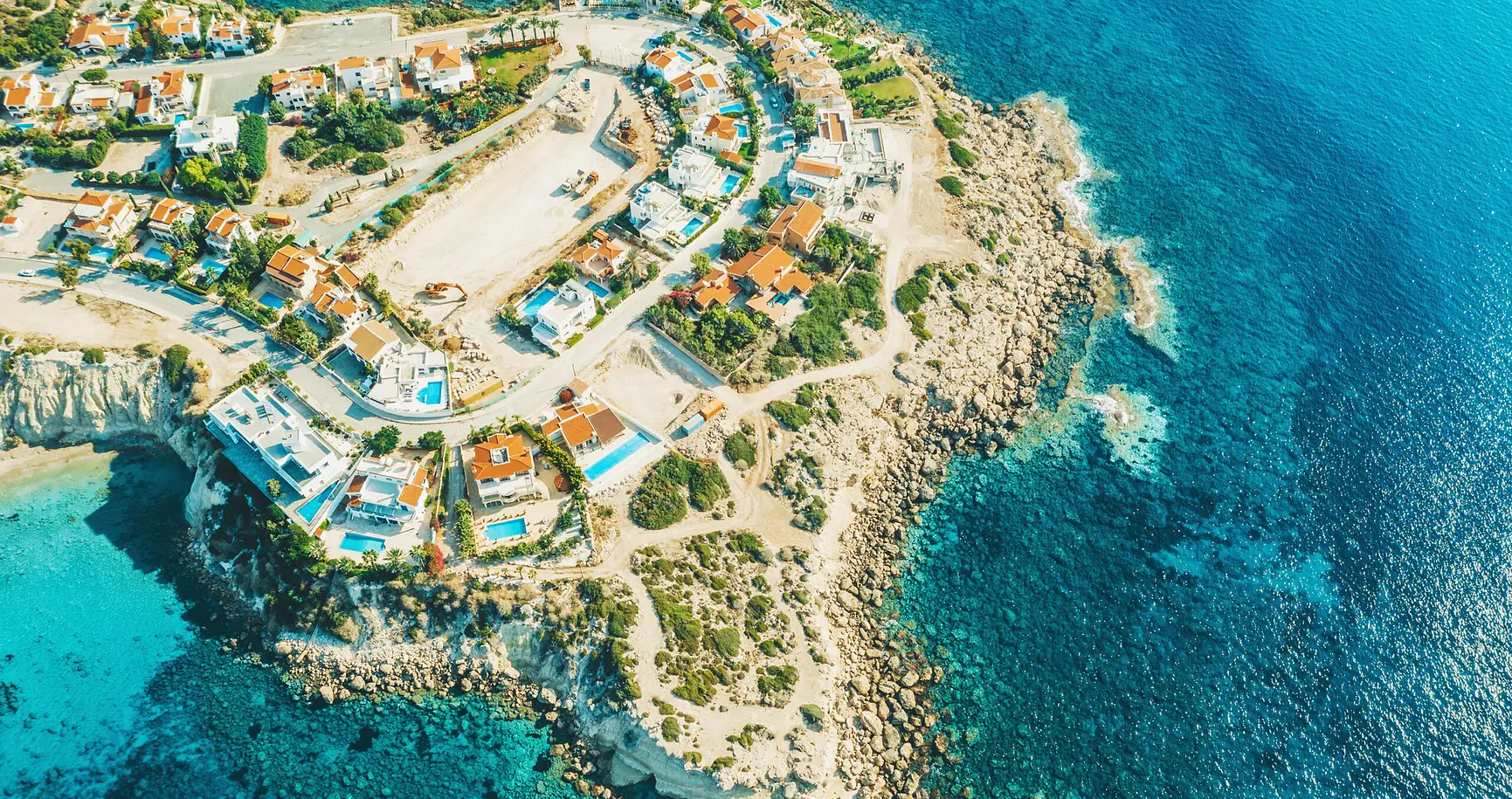 Aerial view of luxury coastal villas with pools on rocky shoreline in Cyprus for property investment opportunities