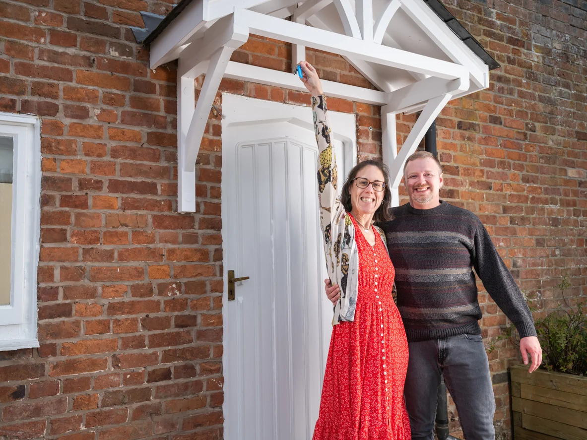 Couple outside brick home holding keys symbolising social housing investment mission and hands free property investment opportunities UK