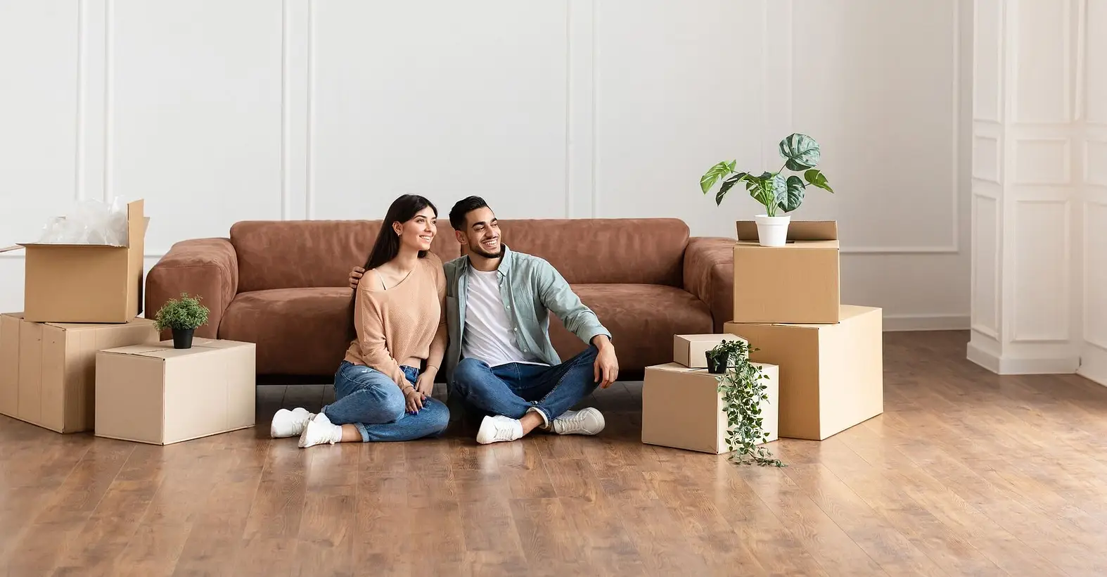 Couple sitting on floor among boxes in new home showing property lettings and management services UK for rental investors