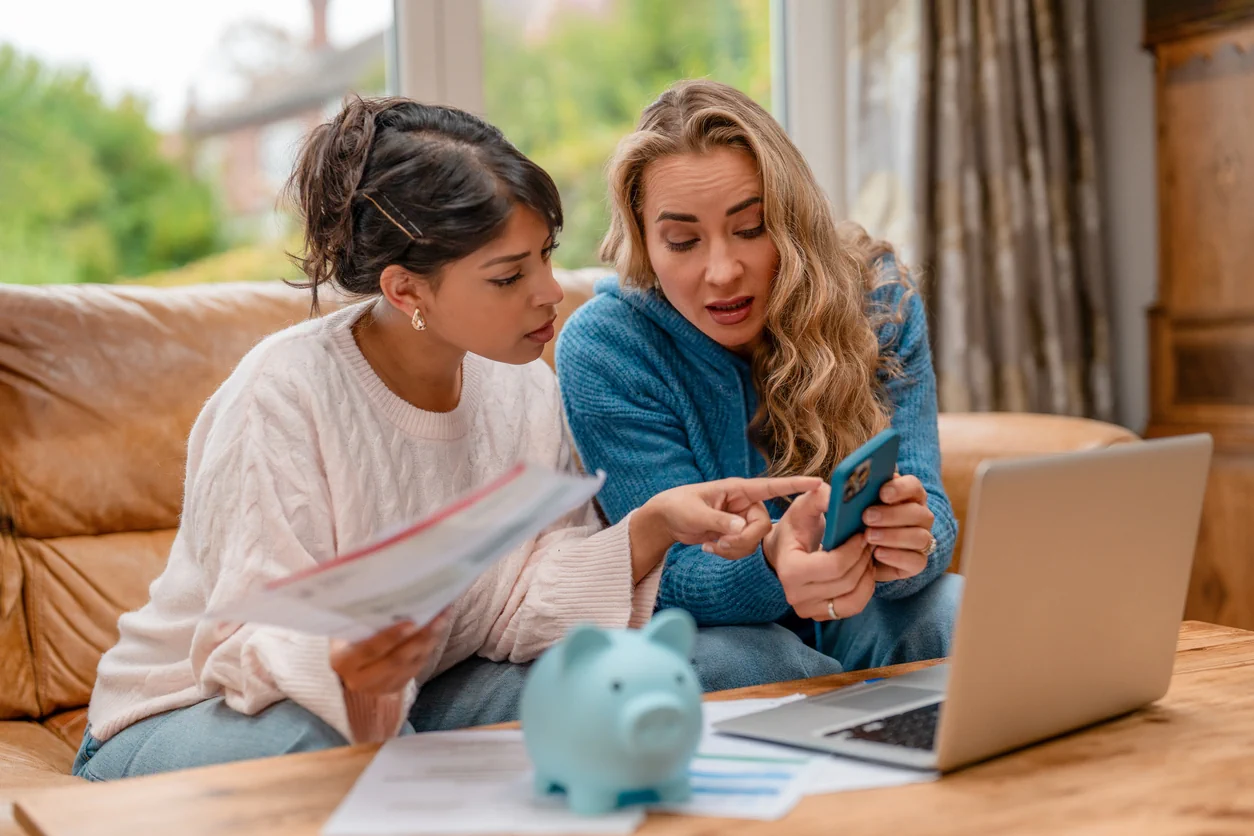 Two women reviewing finances with laptop phone and documents illustrating property investment planning and informed decision making in the UK