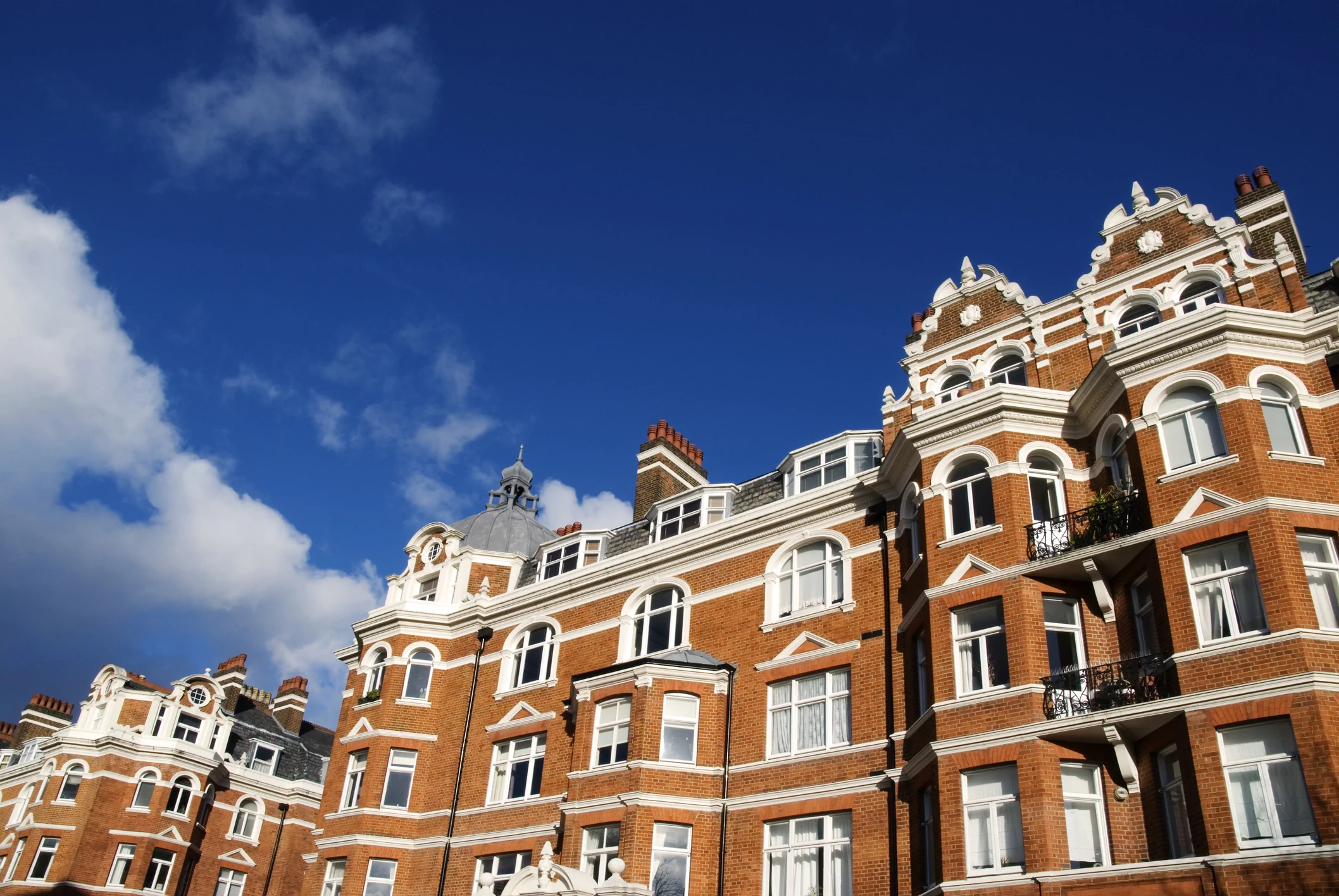 Red brick Victorian apartments with ornate detailing under blue sky representing UK property investment resources and housing market insights