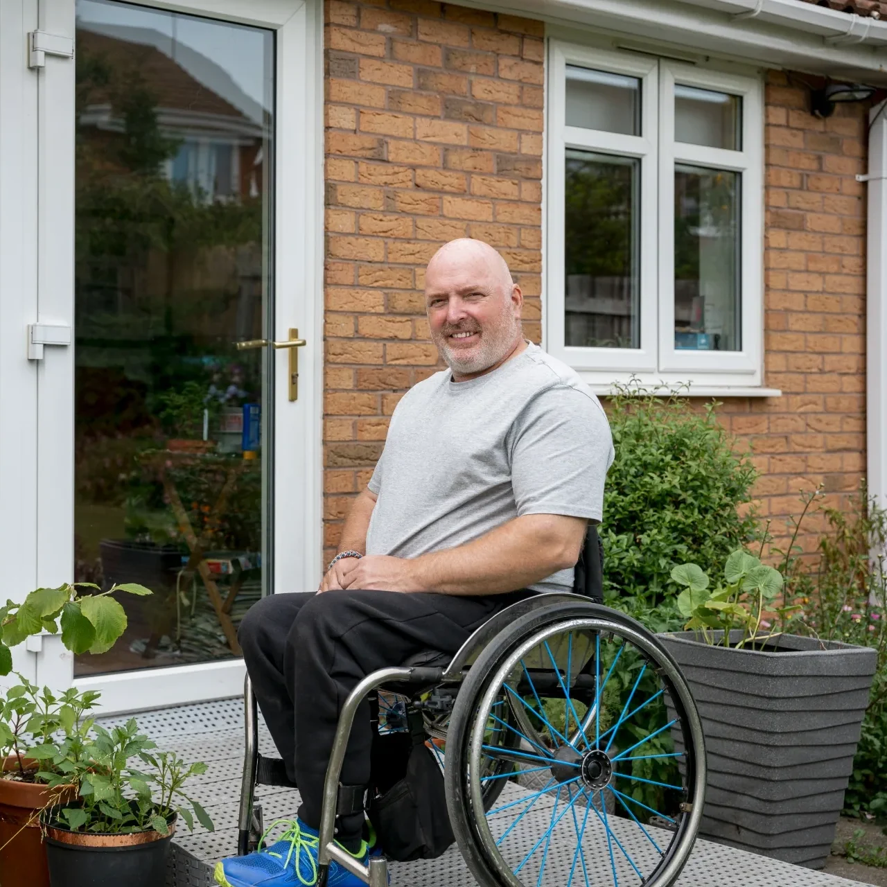 Man in wheelchair outside brick home with ramp access illustrating supported housing and accessible UK property investment options
