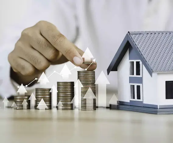 Hand stacking coins beside house model showing currency exchange for overseas property investment and rising UK property values