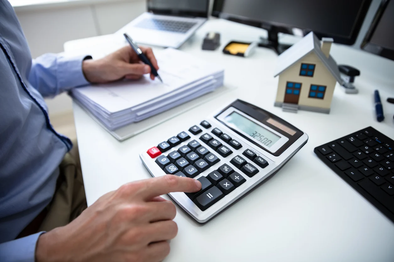 Property investment workspace with calculator documents and house model illustrating exploring investment scenarios and financial planning